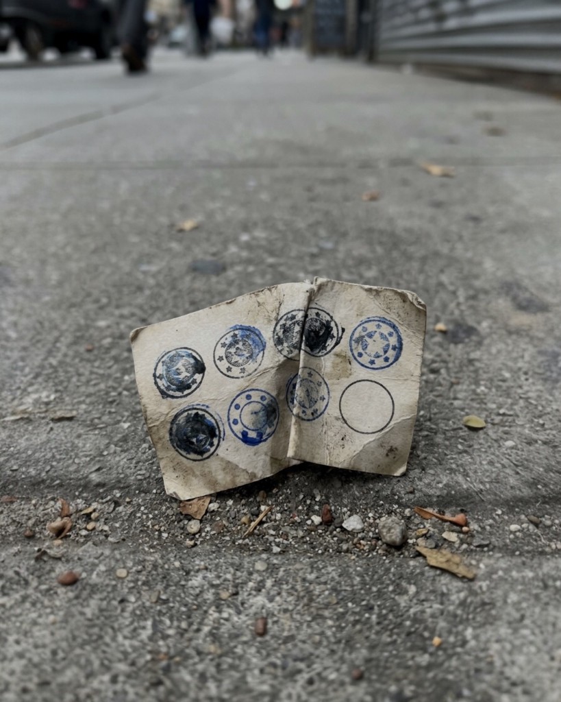 Tarjeta de lealtad de papel arrugada en la acera, casi completa de sellos, como si se hubiera perdido antes del premio.